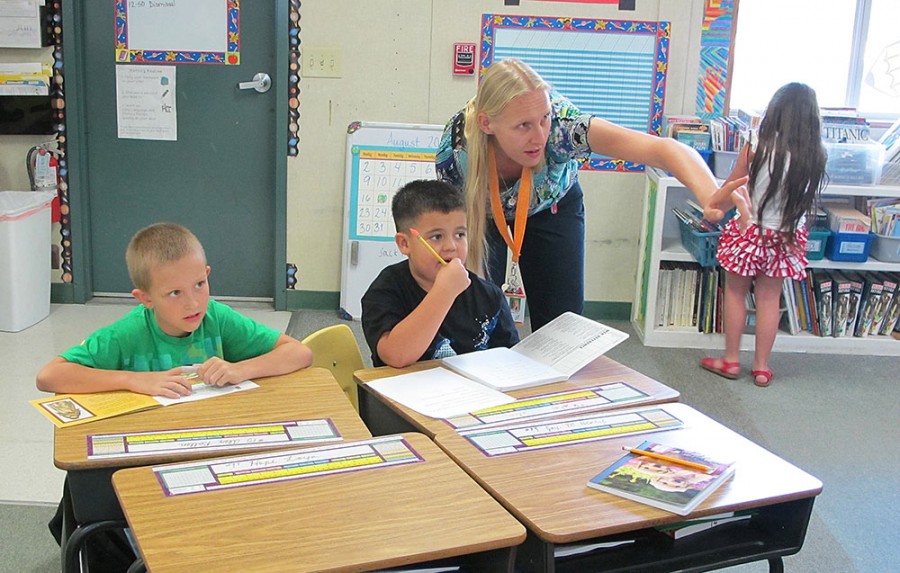 Alex (in green) enjoys free-reading while Shae (in black) finishes a writing assignment​.​ Principal Patricia Davis shows Shae where the writing process is posted on the classroom wall. Both students are in 3rd grade at Monarch Learning Center. 