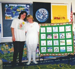 Tami Lavitt with Cindy McPherson stand by a quilt that Tami made from students' drawings to celebrate their love for their teacher who was in love with penguins