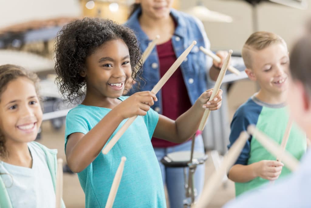 Excited diverse schoolchildren holds drumsticks during percussion class.