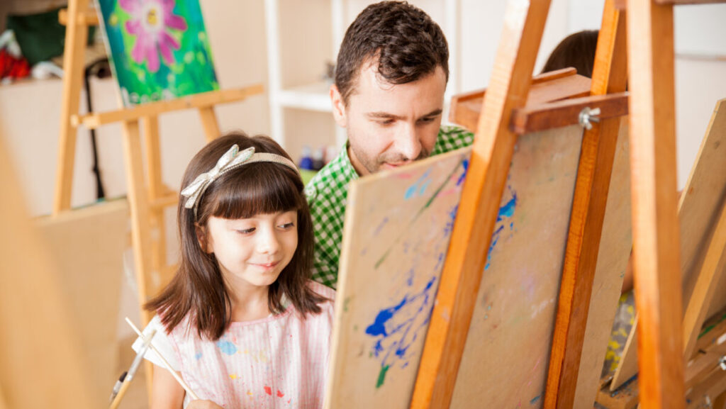 Cute little girl getting help from her teacher during art class at school