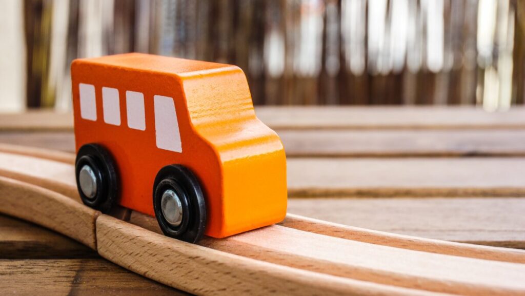 A closeup of an orange wooden toy car on the tracks under the lights with a blurry background