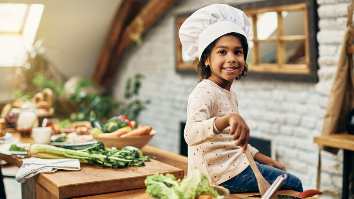 Cute black girl wearing chef’s hat while preparing scrambled egg