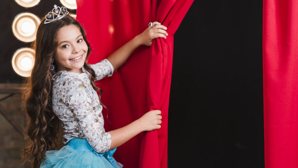 smiling-girl-wearing-crown-opening-red-curtain