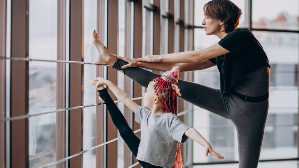 Mother with little daughter practicing yoga by the window