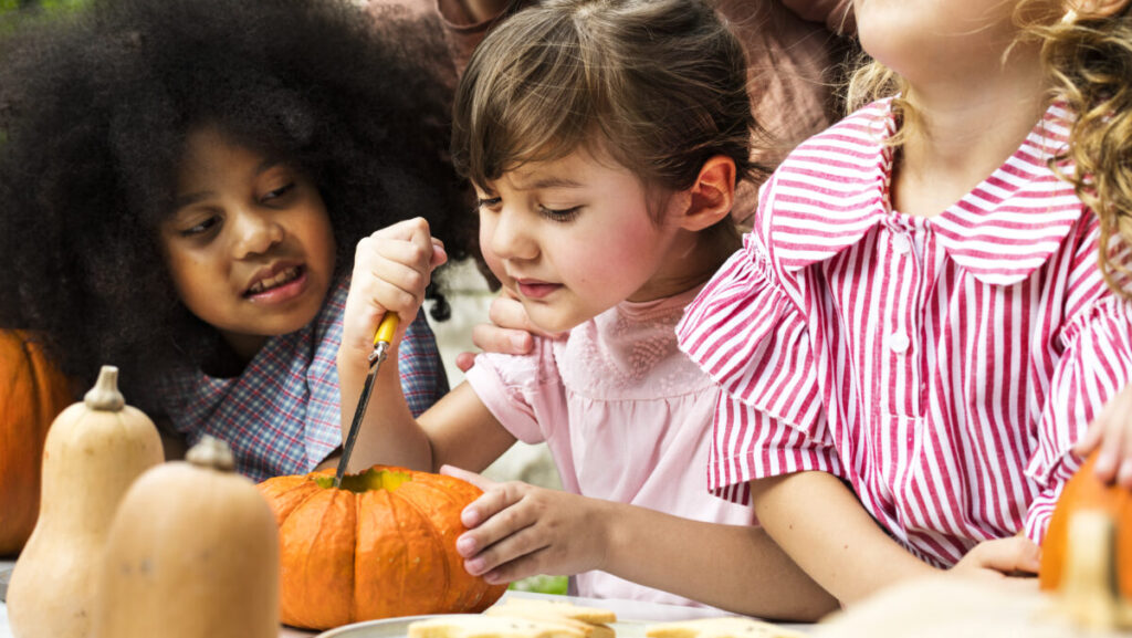 Young kids carving Halloween jack-o-lanterns
