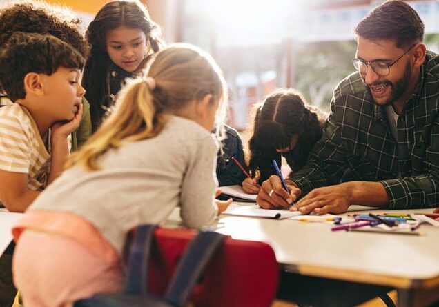 Group of elementary school kids stand around a table in a classroom, attentively following a lesson being taught by their teacher. Young students engaging in a fun activity of colouring and drawing.