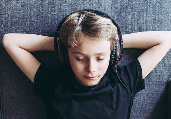 Top view of blonde boy listening to music with headphones closed