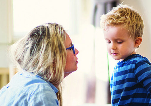 A young mother talking to her sad toddler son inside in a bedroom.